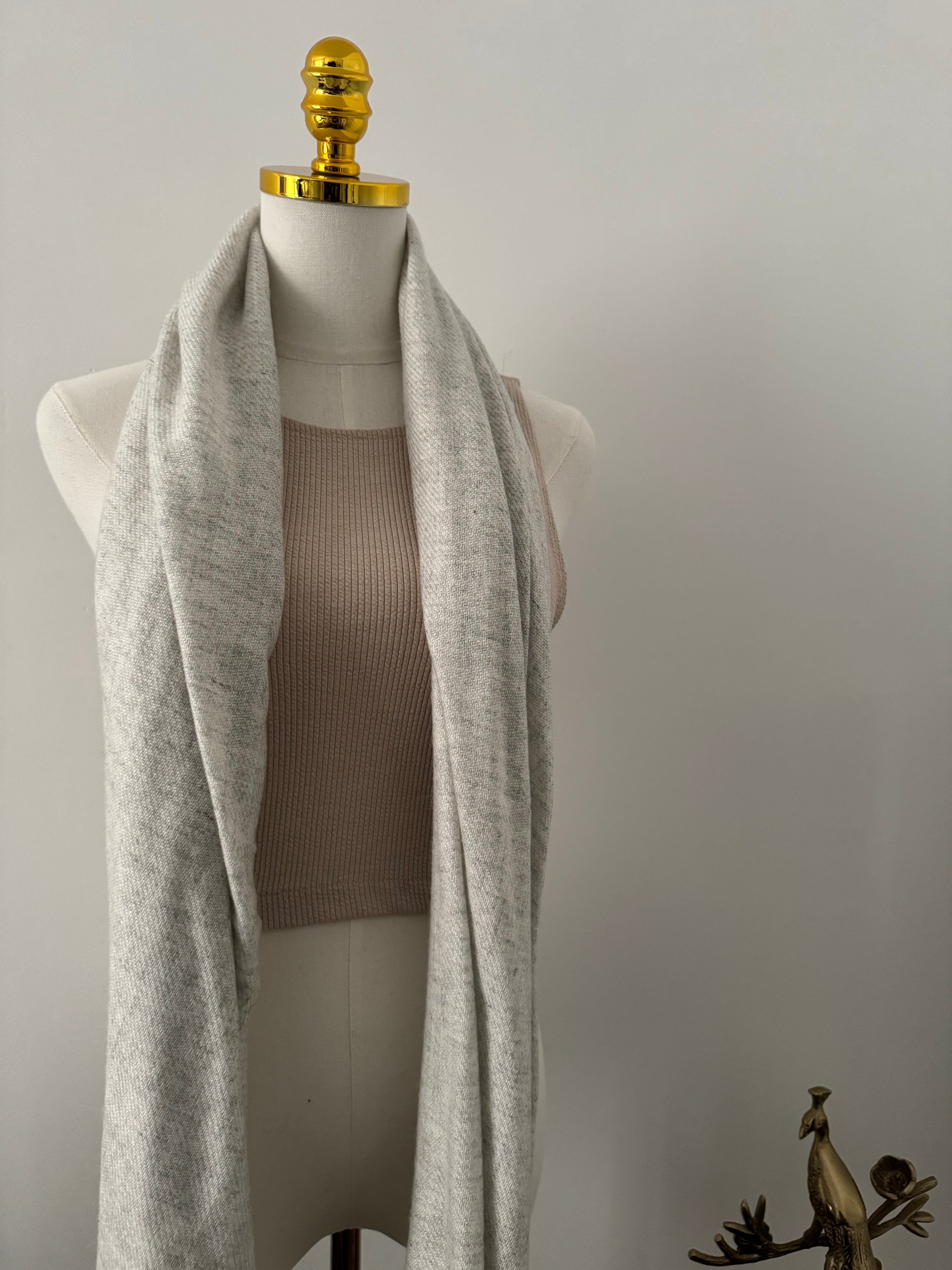 Mannequin wearing a light gray fabric with a gold decorative element on a plain background