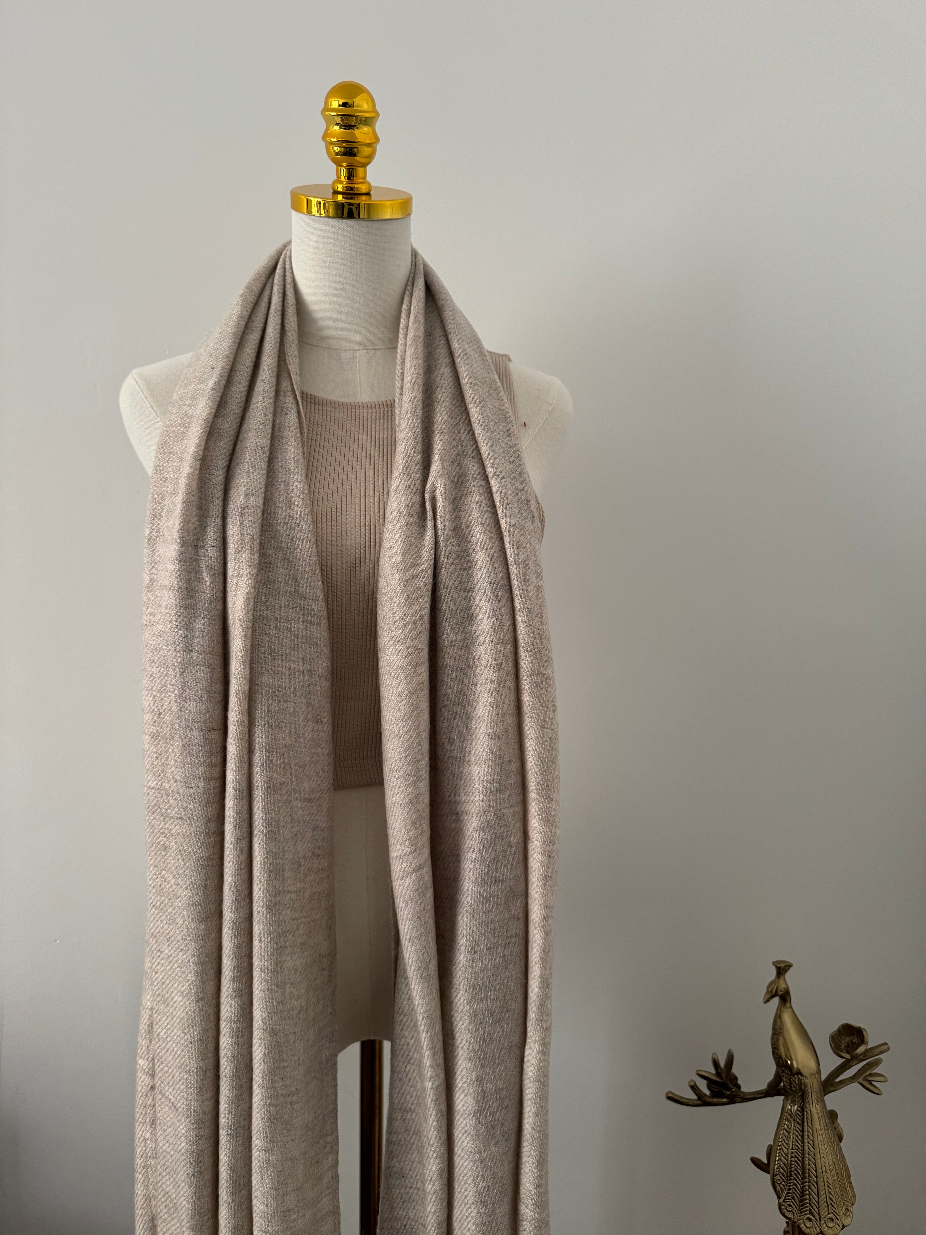 Mannequin wearing a beige shawl on a plain background