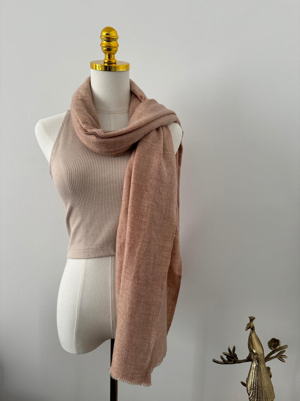 Mannequin wearing a beige scarf with a gold decorative element on a plain background