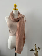Mannequin wearing a beige scarf with a gold decorative element on a plain background