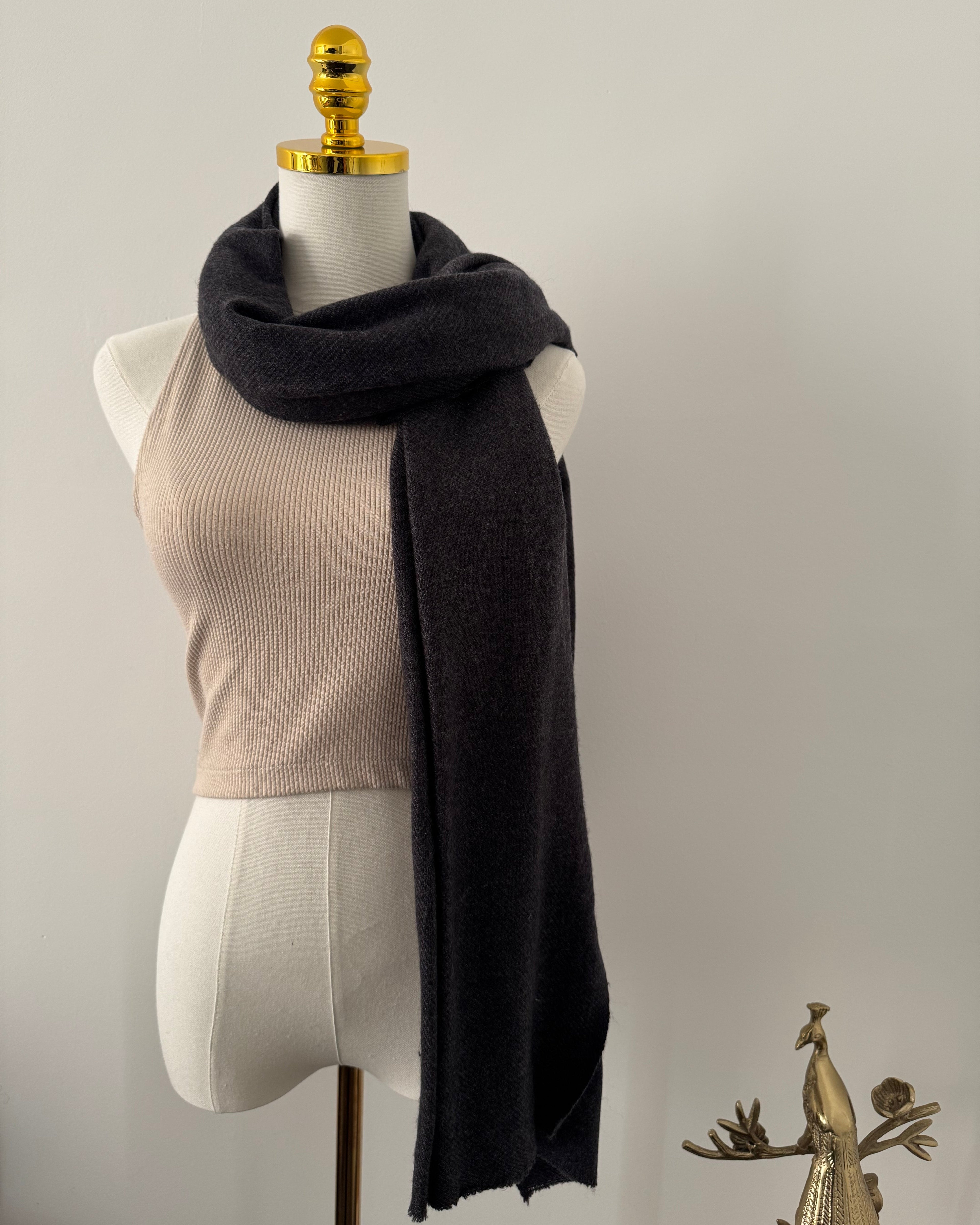 Mannequin wearing a black scarf with a gold decorative element on a plain background