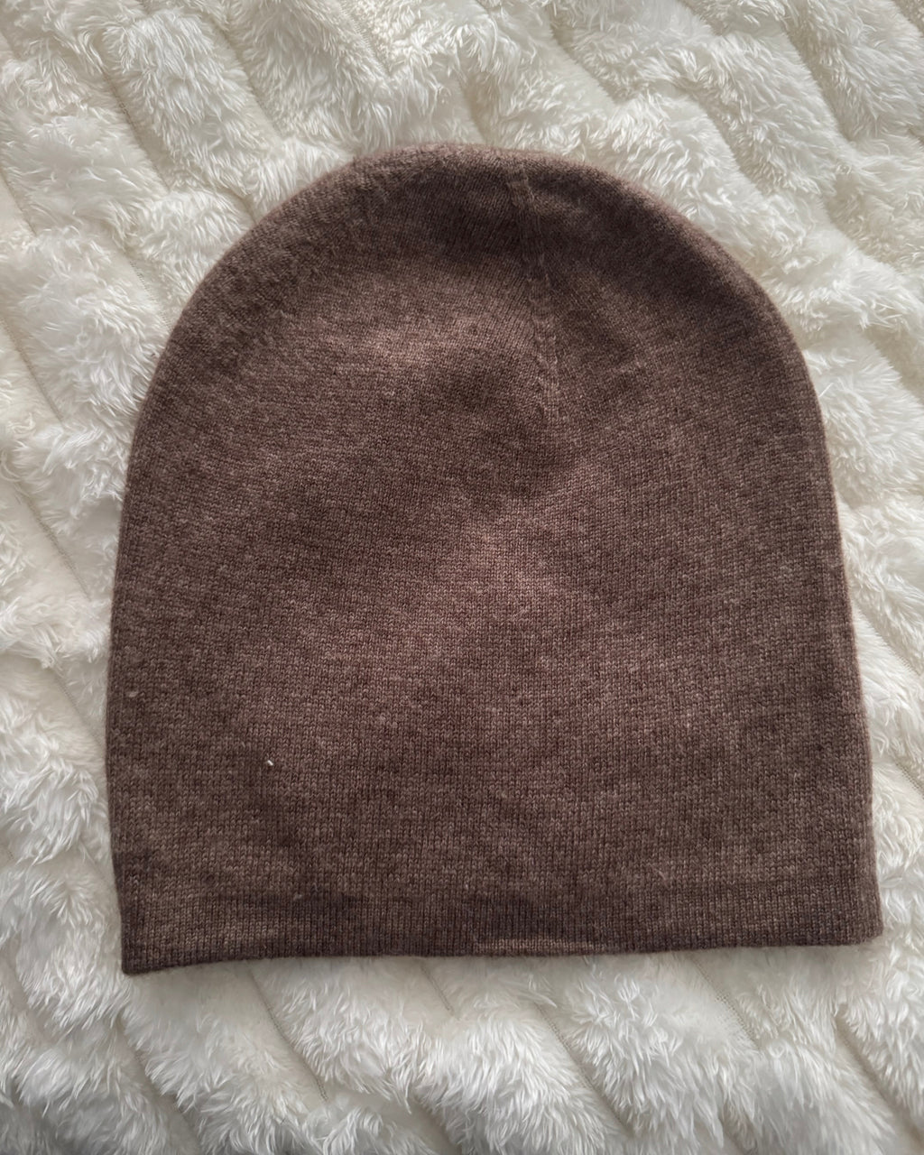 Brown knitted beanie on a textured white surface