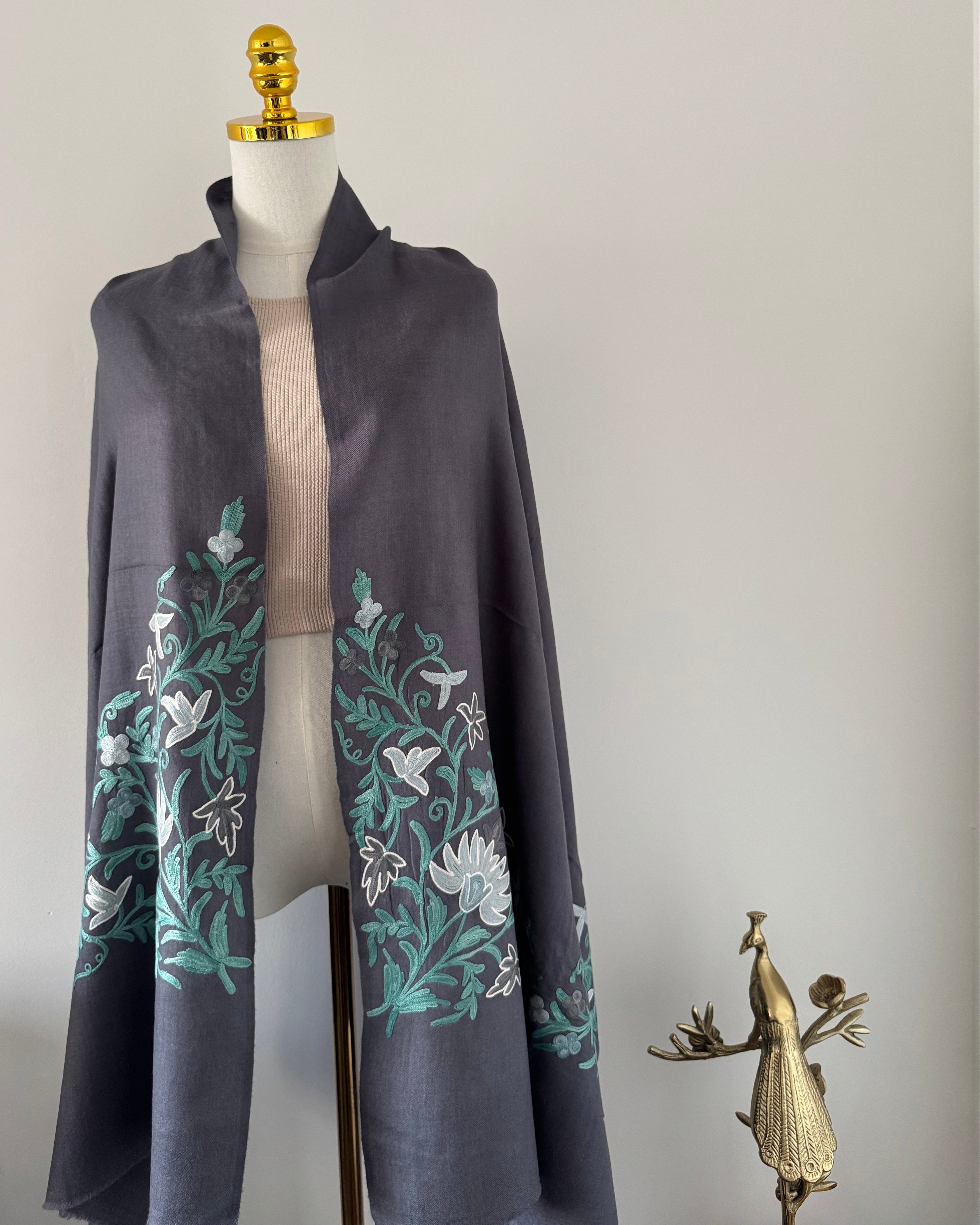 Dark gray fabric with floral embroidery on a mannequin against a light gray background