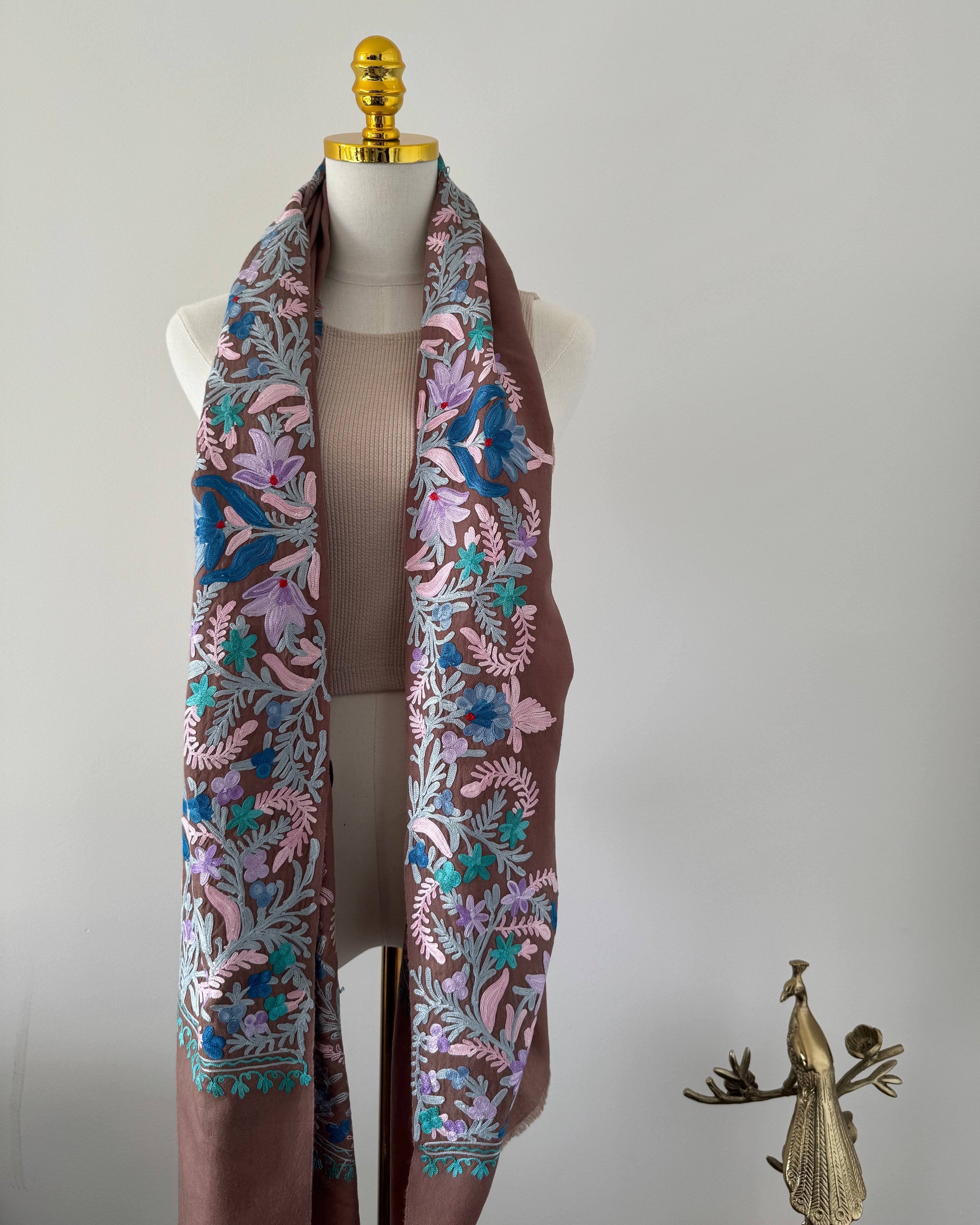 Mannequin wearing a brown scarf with floral patterns on a plain background