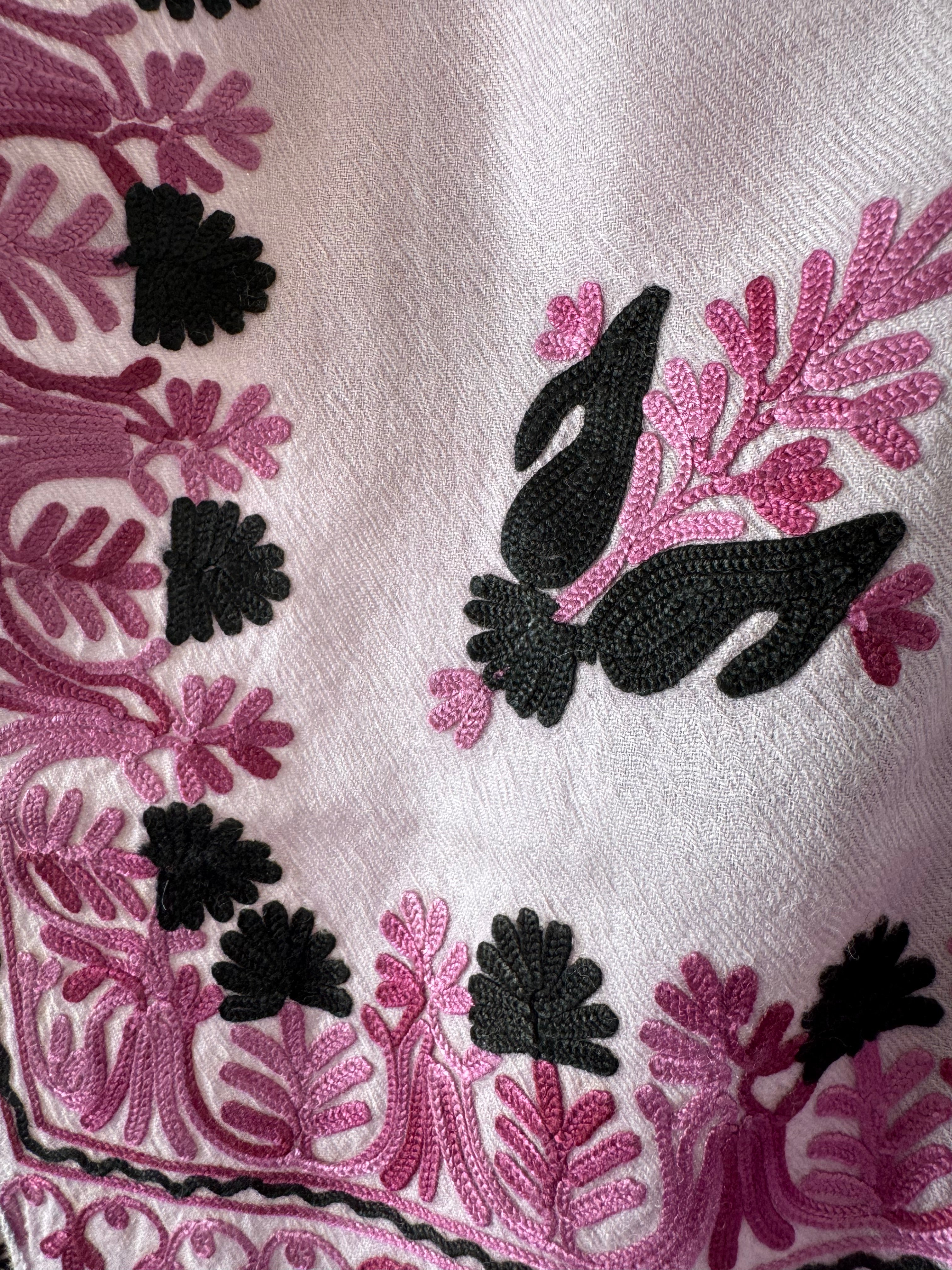 Close-up of embroidered fabric with pink and black floral patterns on a white background