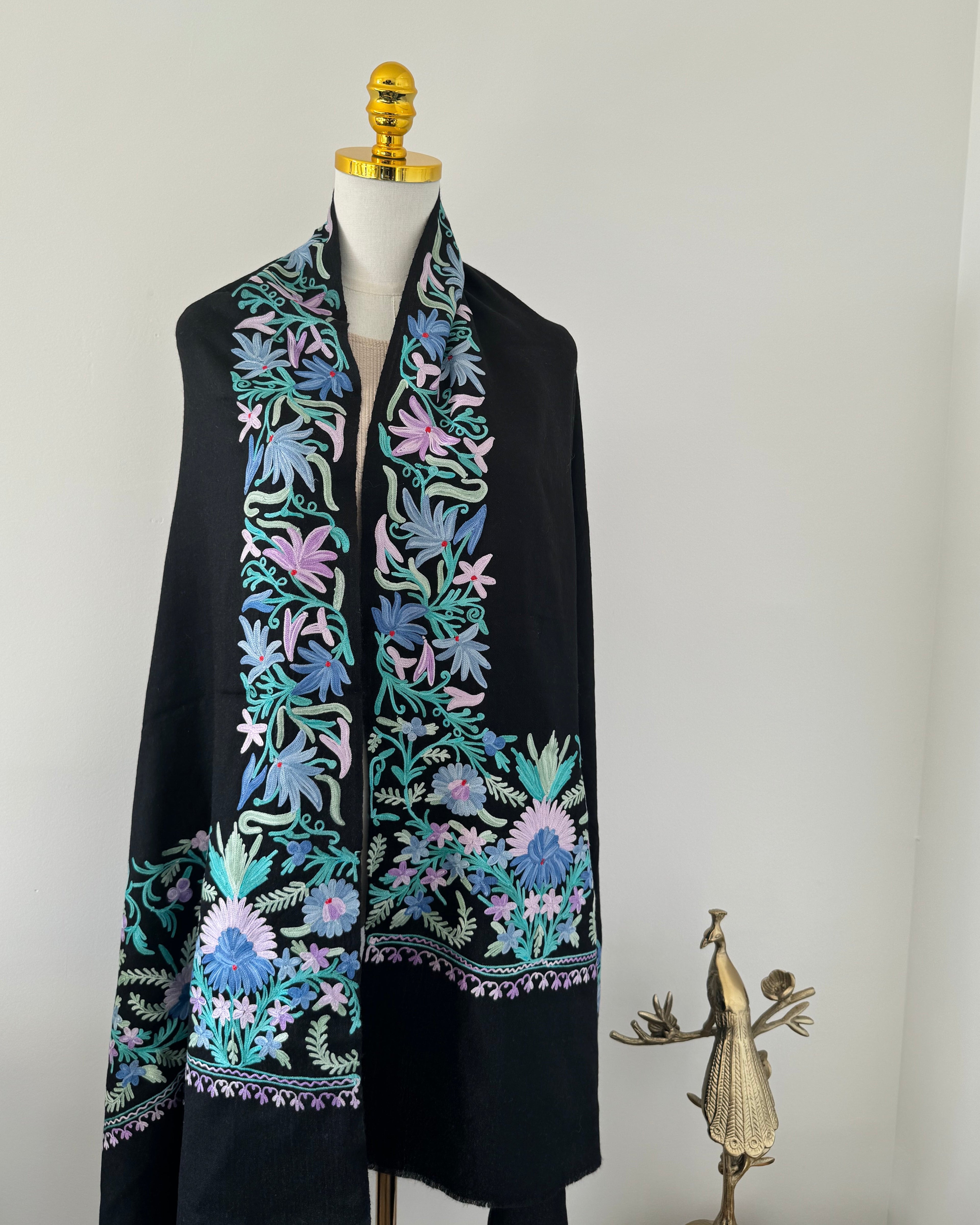 Black shawl with colorful floral embroidery on a mannequin against a plain background