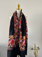 Black shawl with colorful floral embroidery on a mannequin against a plain background