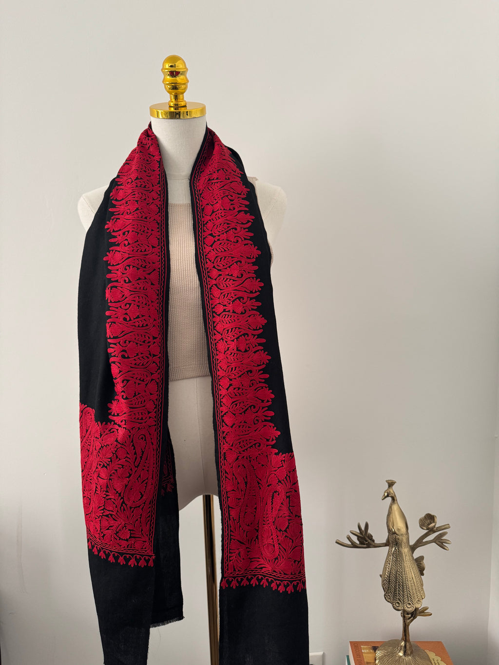 Red and black embroidered garment on a mannequin against a plain background