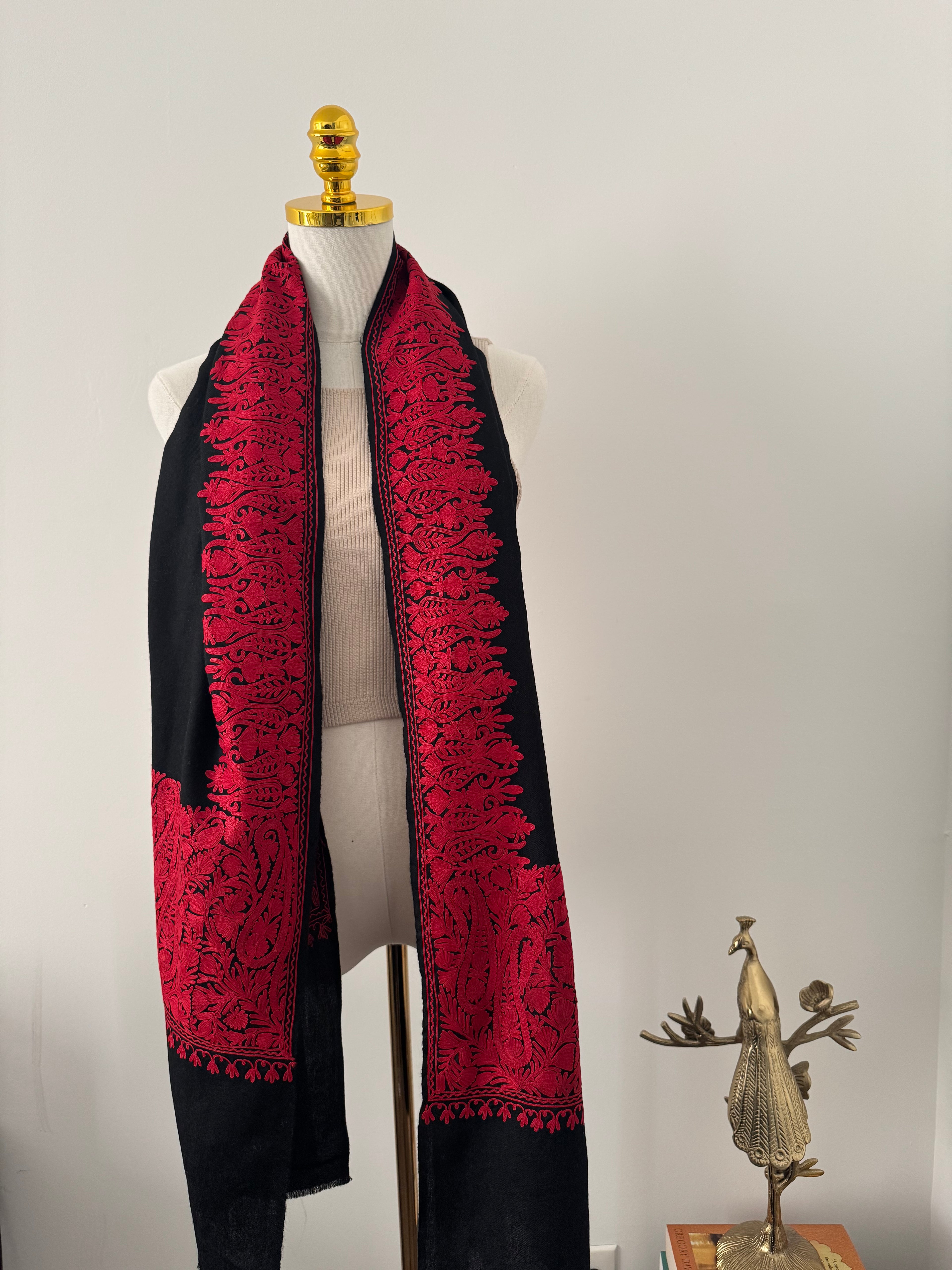 Red and black embroidered garment on a mannequin against a plain background