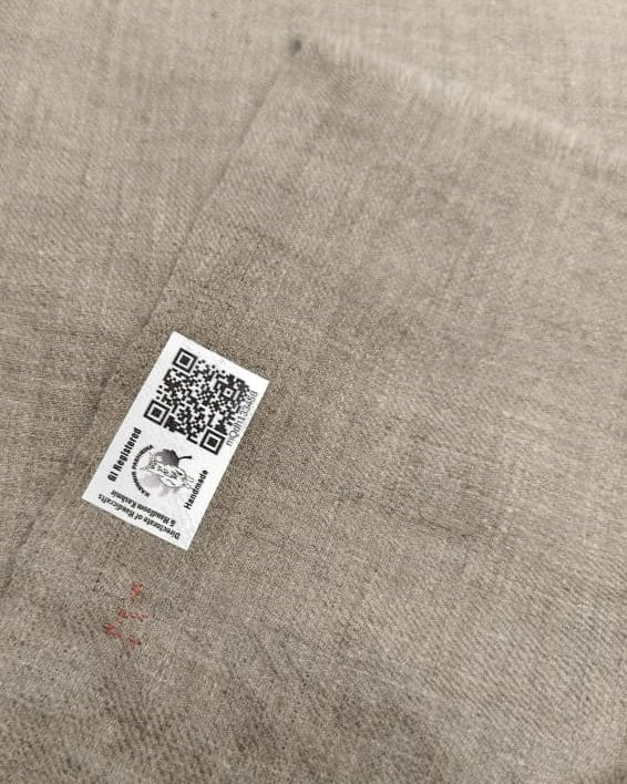 Close-up of a QR code label on beige fabric with a visible brand logo.