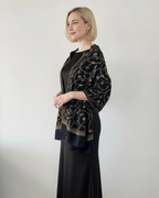 Woman wearing a black dress with a gold embroidered shawl against a white background
