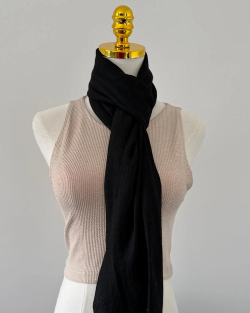 Mannequin wearing a beige top and black scarf with a gold knob on a gray background