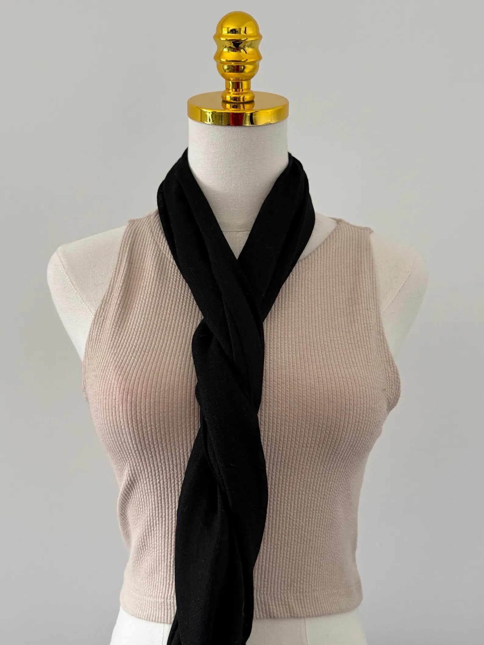 Mannequin wearing a beige sleeveless top with a black scarf draped over it on a gray background