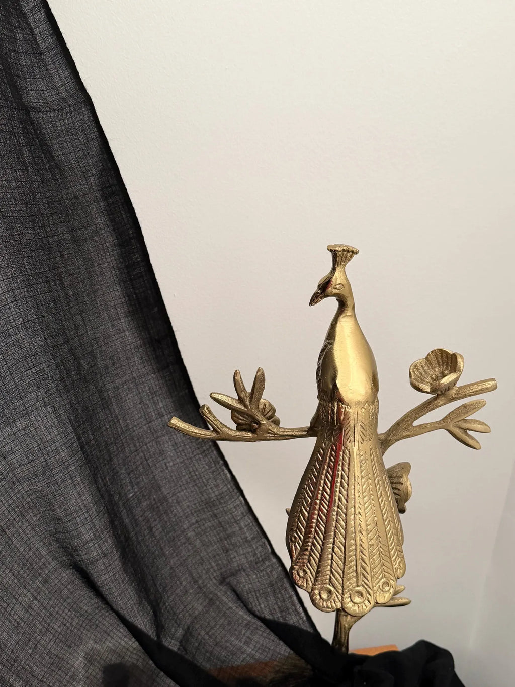 Gold peacock decorative item against a gray curtain background