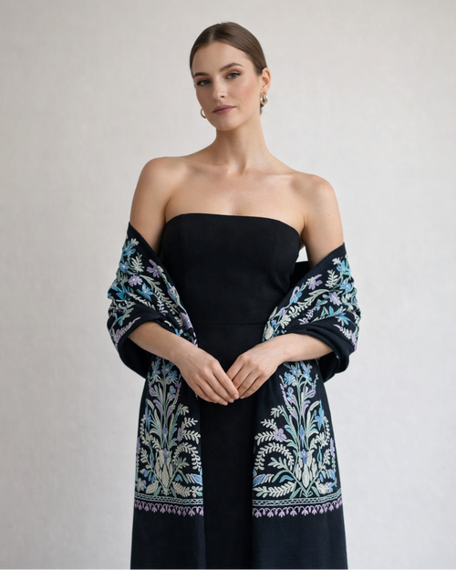 Woman wearing a black strapless dress with a floral patterned shawl on a plain background