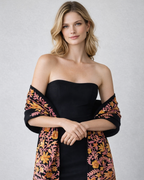 Woman wearing a black strapless dress with a floral embroidered shawl on a plain background