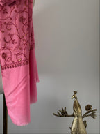Pink scarf with embroidery next to a gold peacock figurine on a light gray background