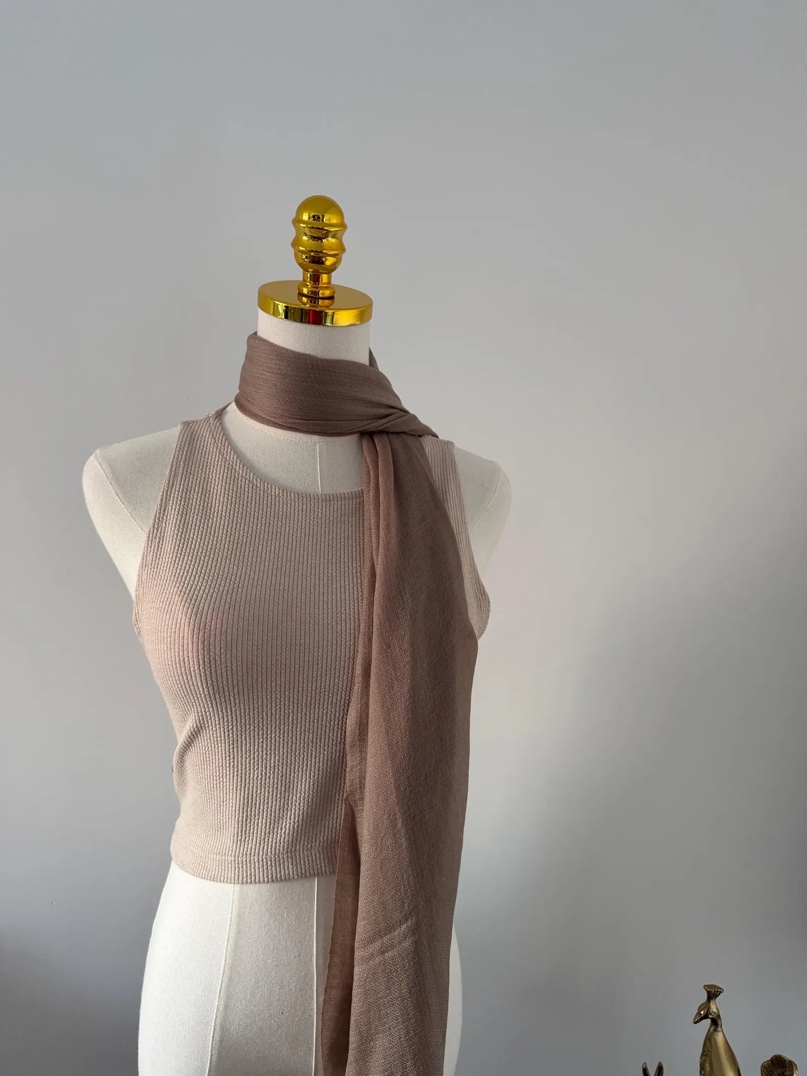 Mannequin wearing a beige ribbed top and brown scarf against a gray background