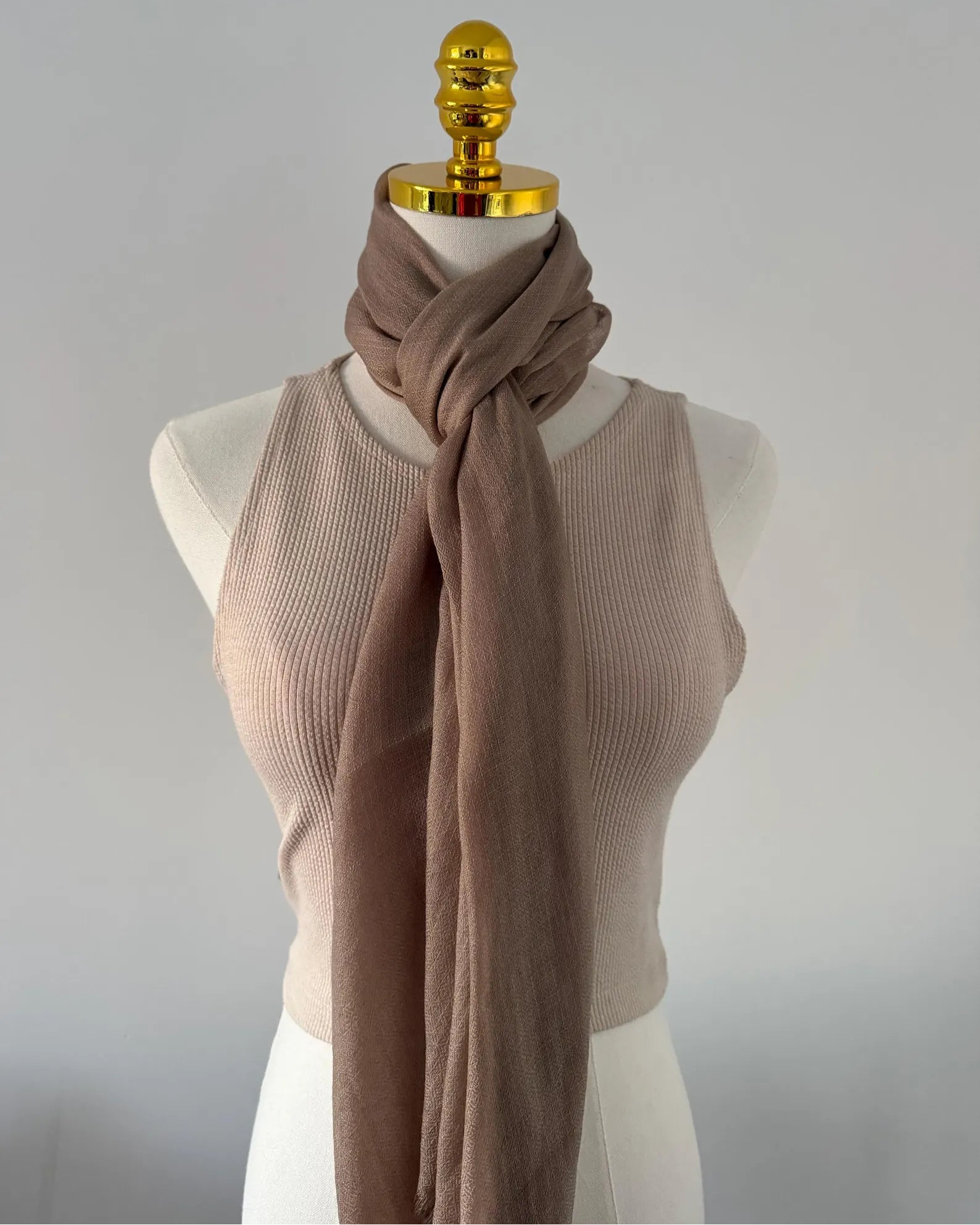 Mannequin wearing a beige sweater and brown scarf against a plain background