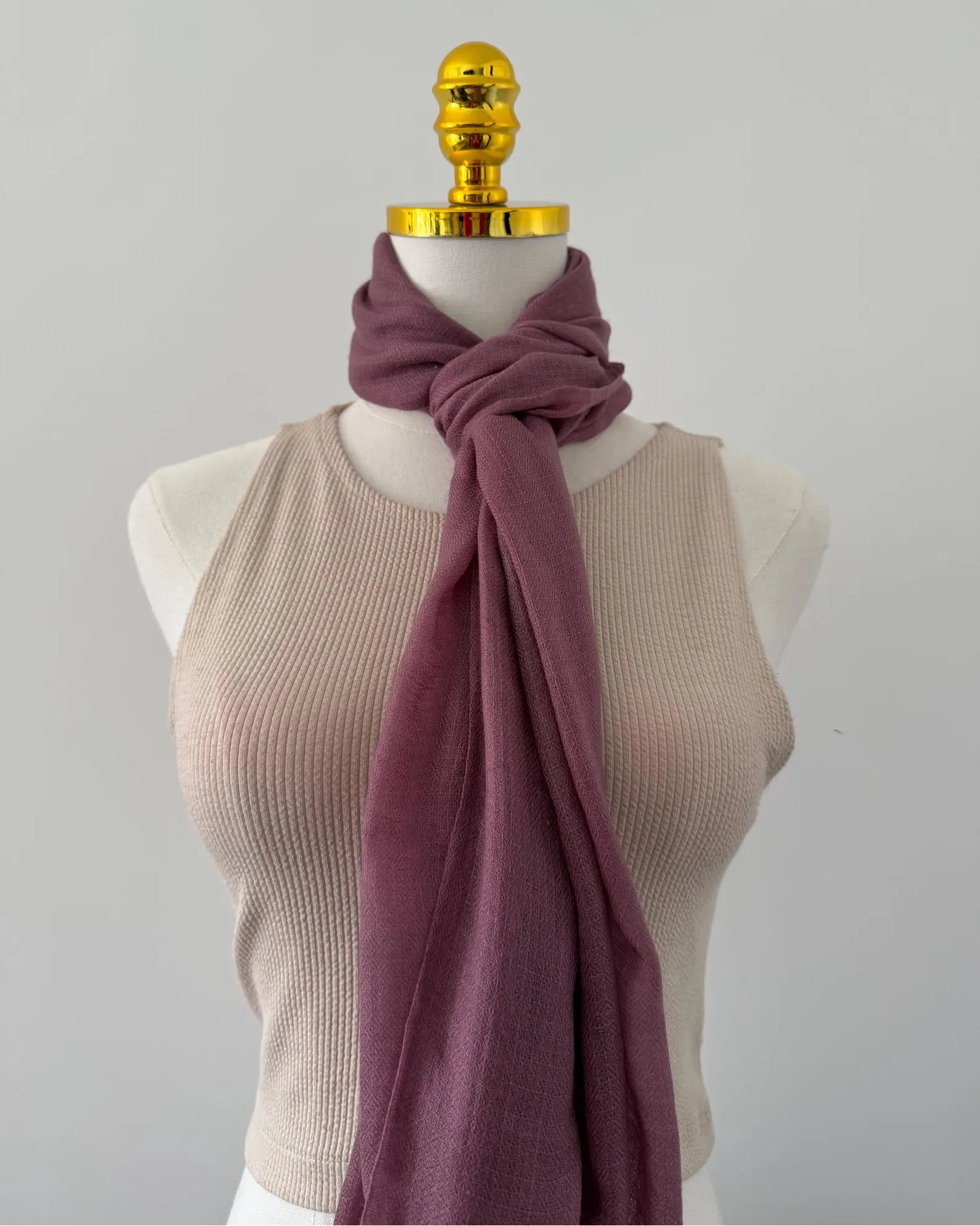 Mannequin wearing a beige tank top and purple scarf with a gold knob on a gray background