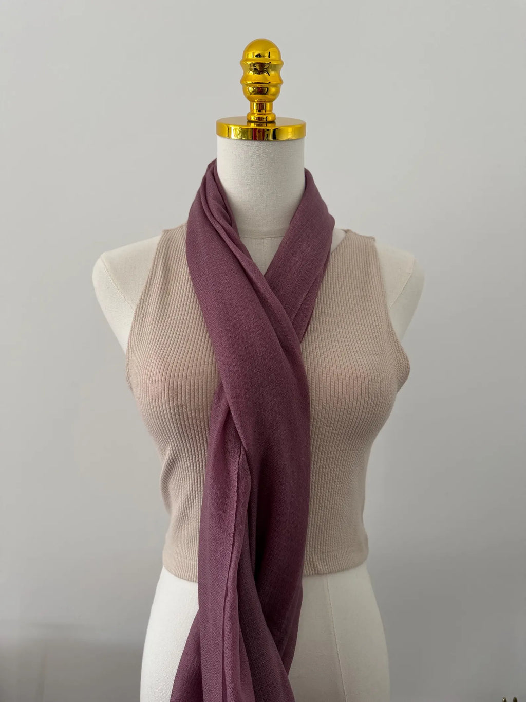 Mannequin wearing a beige sleeveless top with a mauve scarf draped over it on a plain background