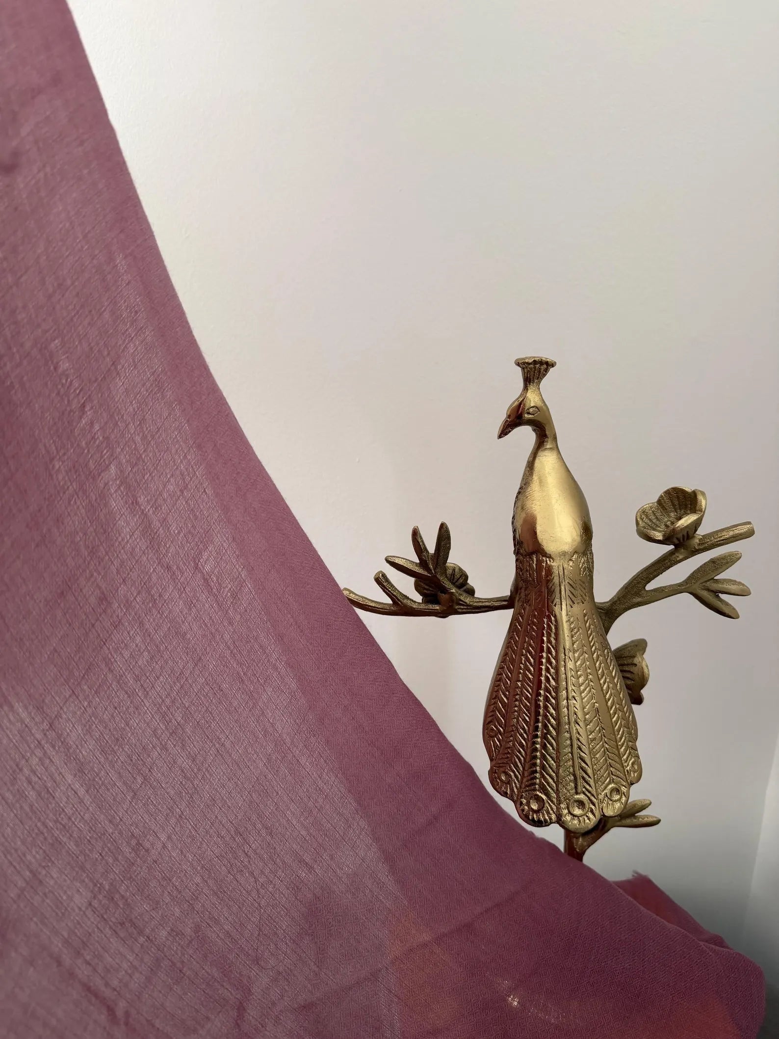 Gold peacock decorative item on a pink fabric background