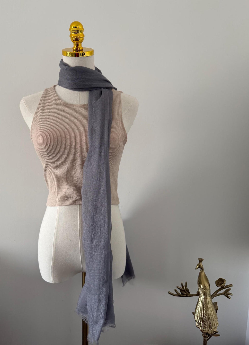 Mannequin wearing a beige top and gray scarf with decorative elements on a plain background