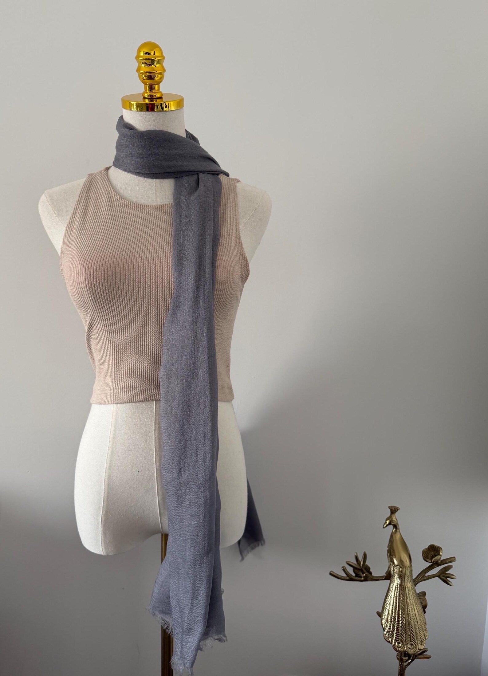 Mannequin wearing a beige top and gray scarf with decorative elements on a plain background