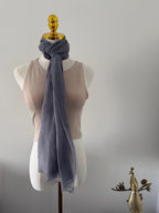 Mannequin wearing a light gray scarf with a gold bird ornament on a plain background