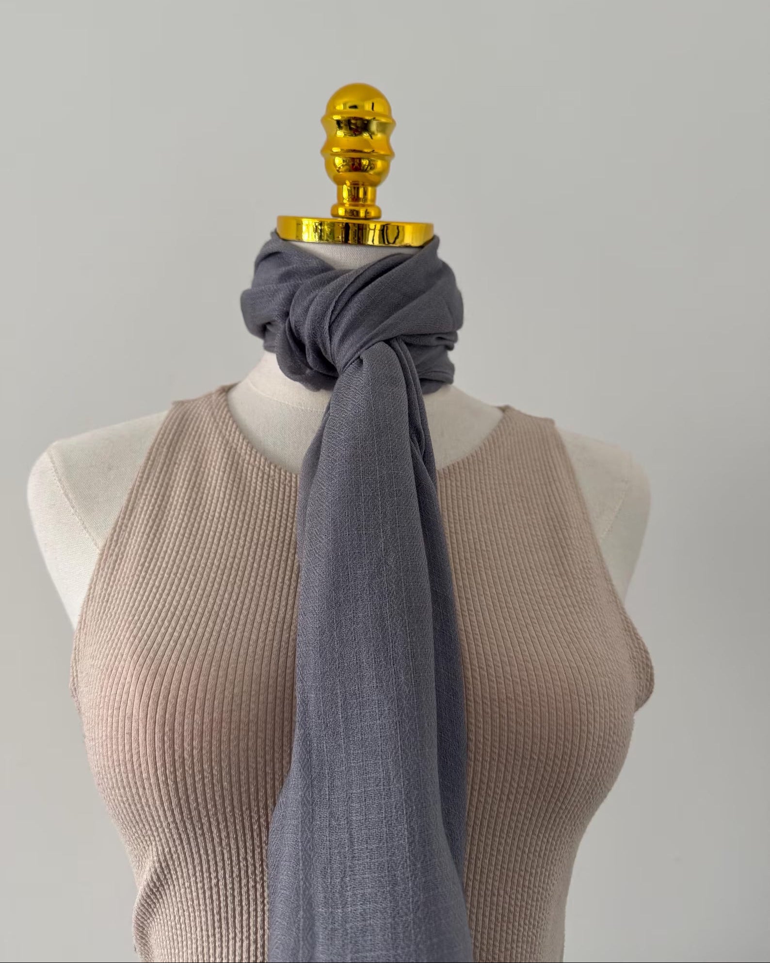 Mannequin wearing a beige ribbed top with a gray scarf draped over it, on a plain background.