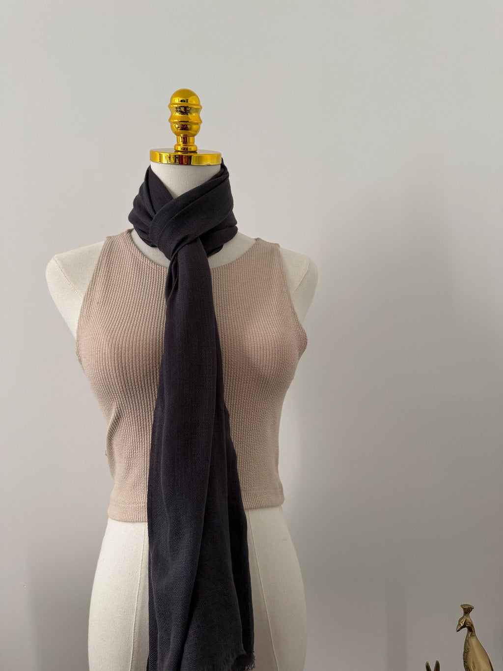 Mannequin wearing a beige top and dark gray scarf against a plain background