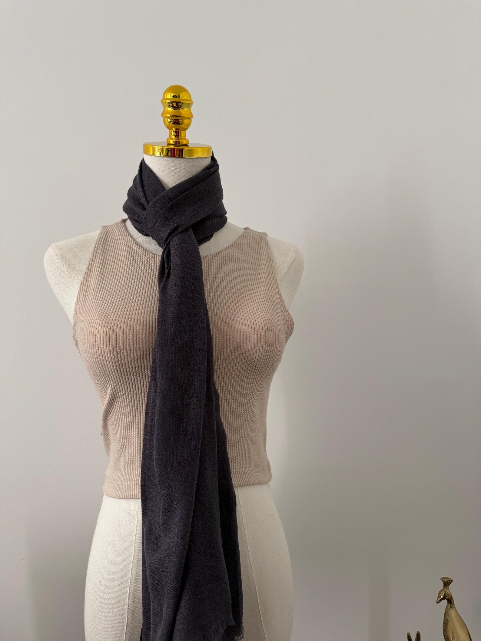 Mannequin wearing a beige top and dark gray scarf against a plain background