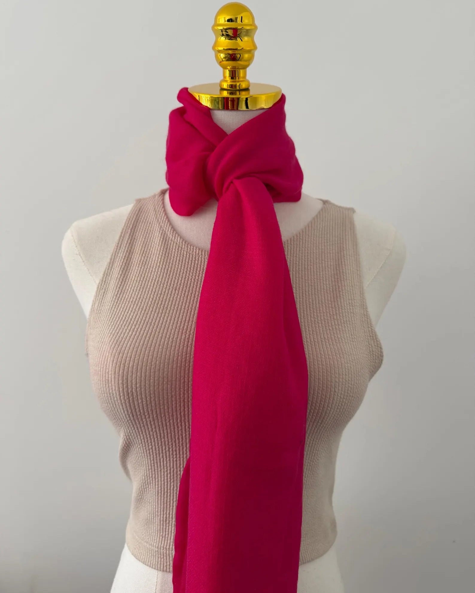 Mannequin wearing a bright pink scarf with a gold top on a plain background