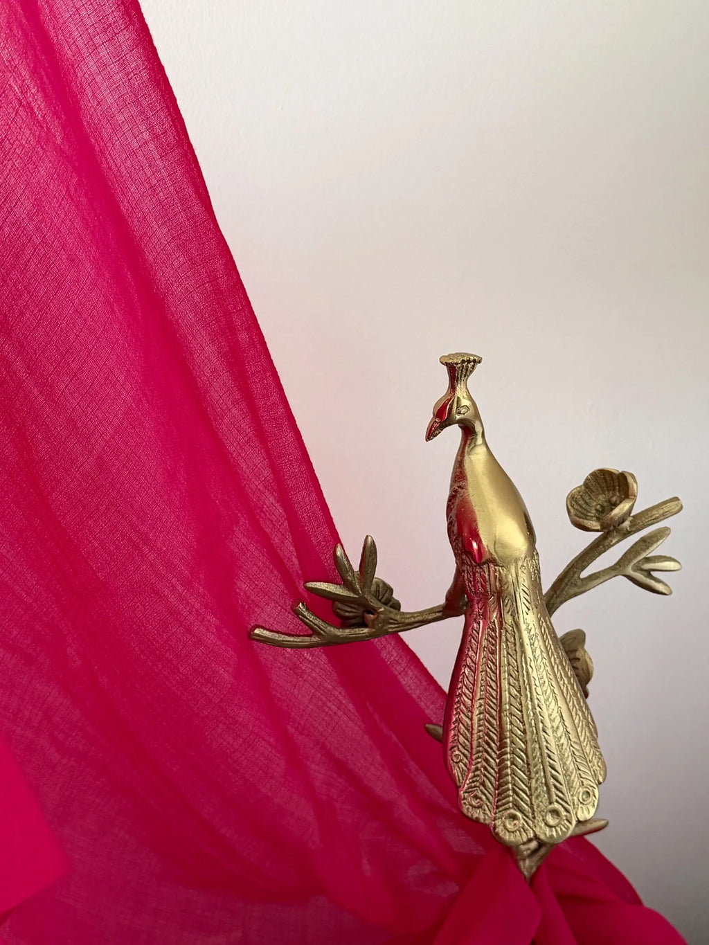 Gold peacock figurine against a pink fabric background