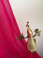 Gold peacock figurine against a pink fabric background