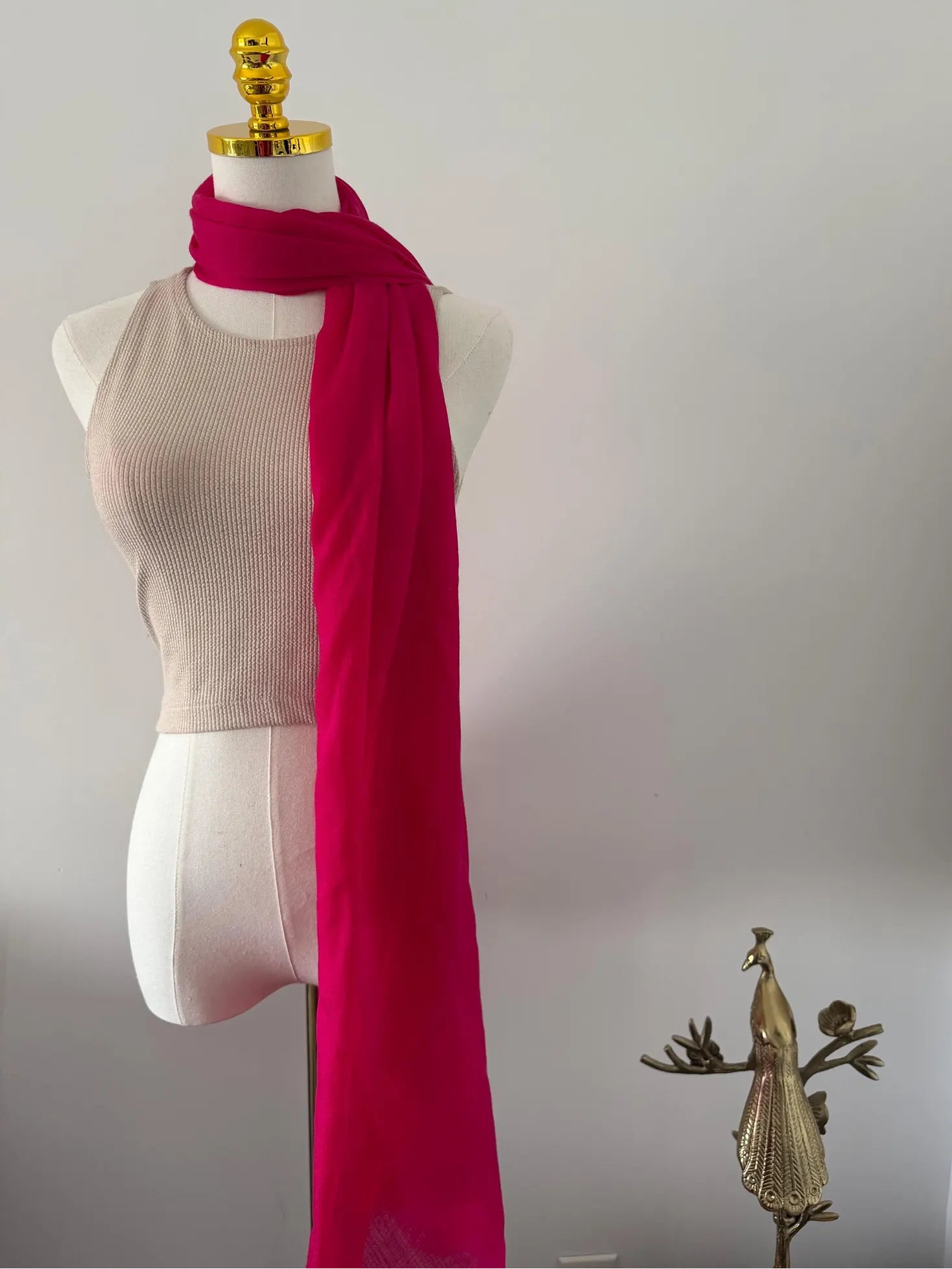 Mannequin wearing a beige top with a bright pink scarf on a plain background