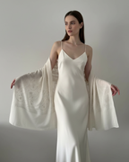 Woman wearing a white slip dress holding a matching shawl against a plain background