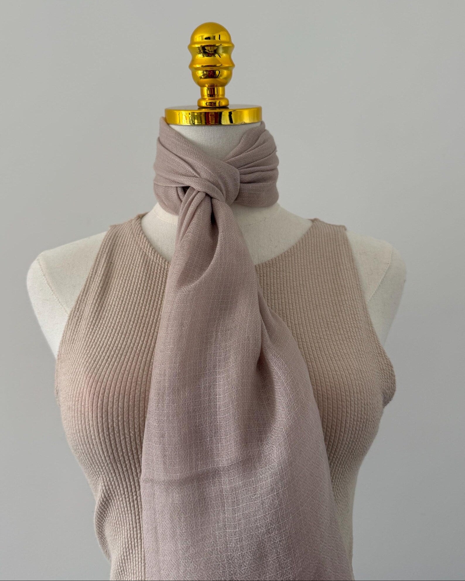 Mannequin wearing a beige scarf with a gold top on a gray background