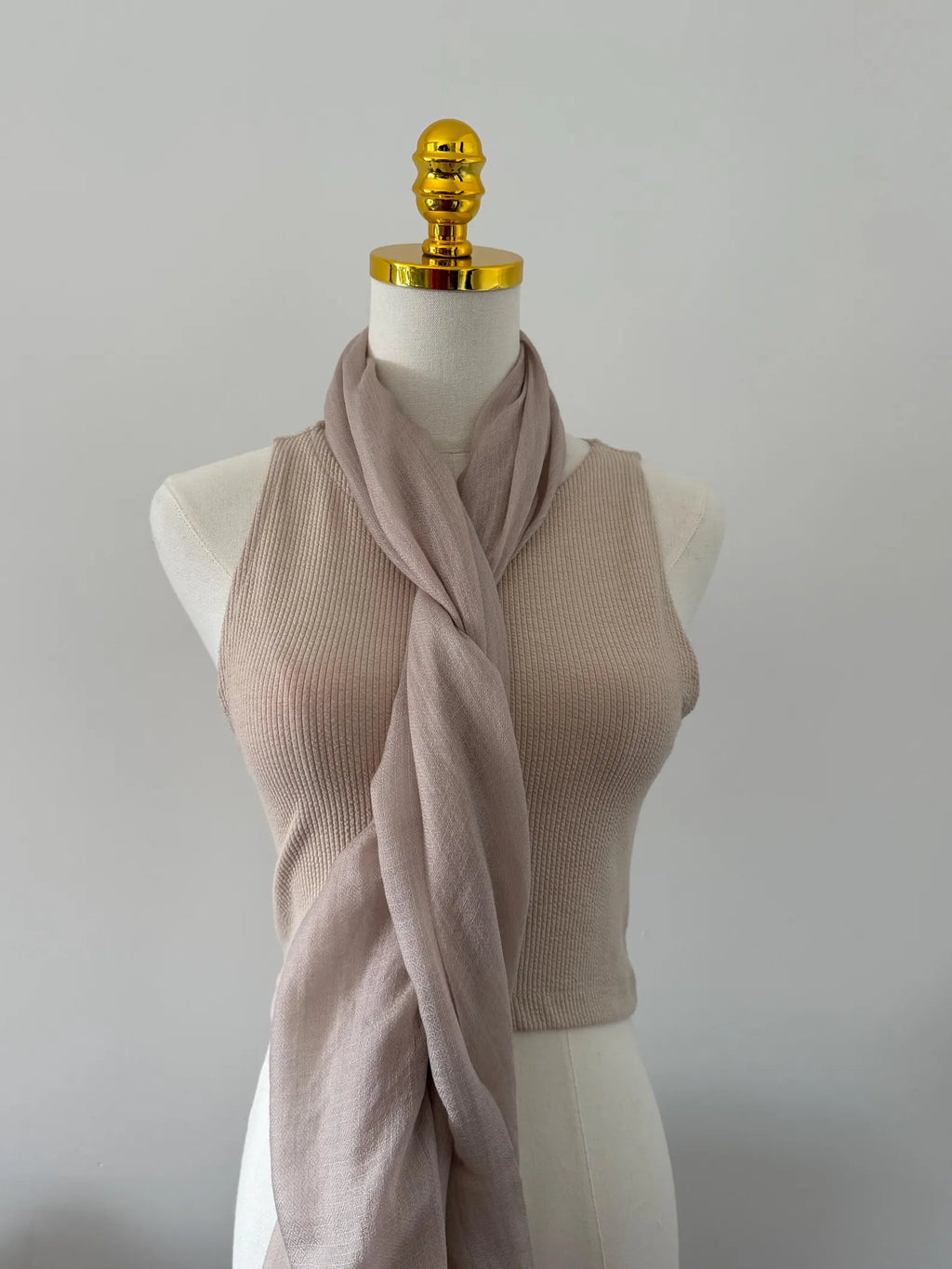 Mannequin wearing a beige ribbed tank top and pink scarf against a plain background