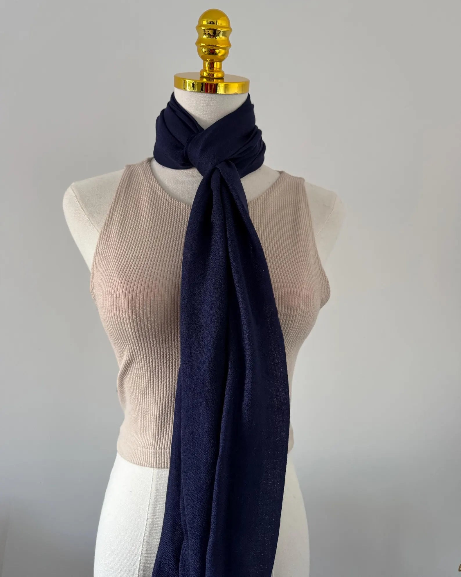 Mannequin wearing a beige top and navy scarf against a plain background
