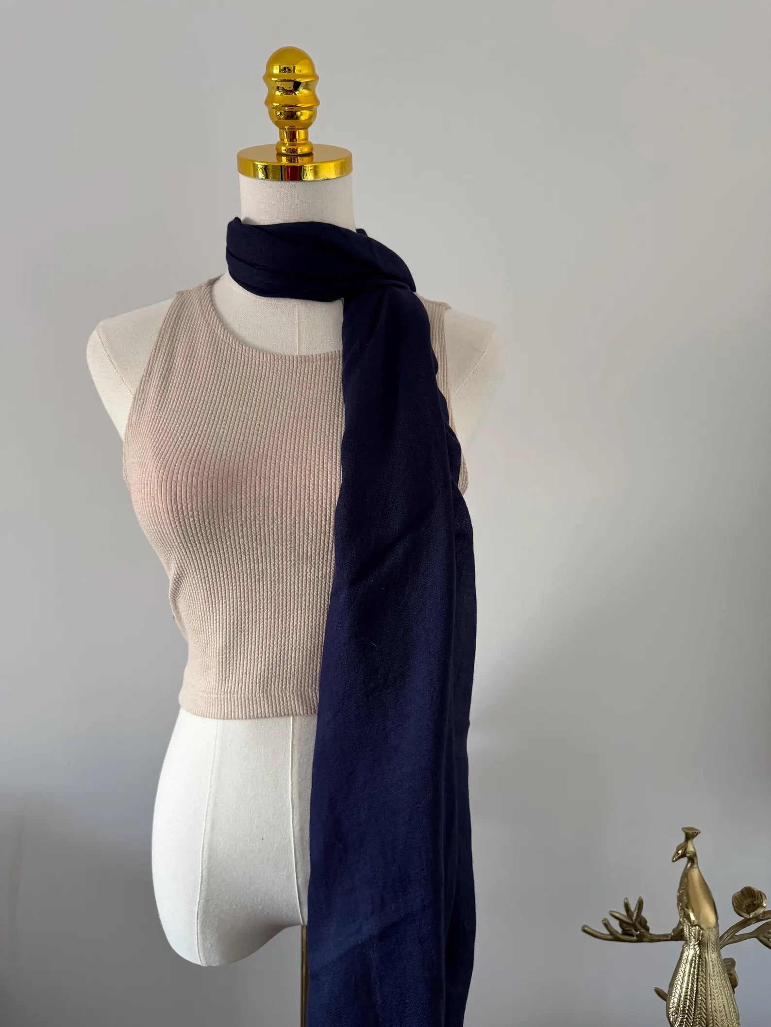 Mannequin wearing a beige top and navy scarf against a plain background