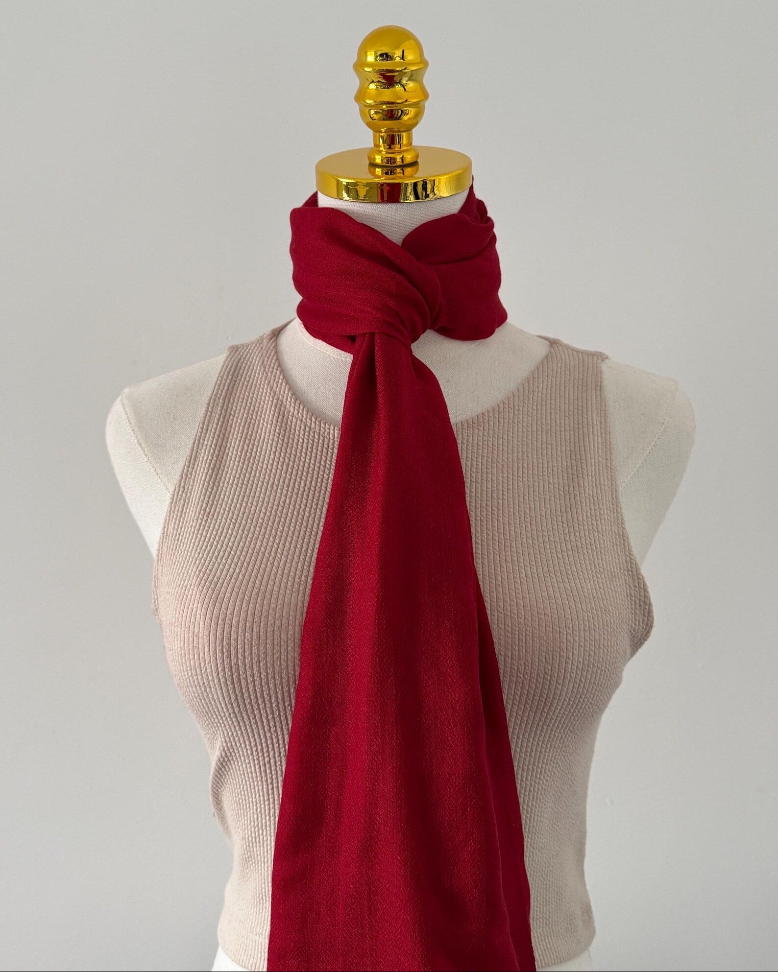 Mannequin wearing a red scarf and beige top against a gray background