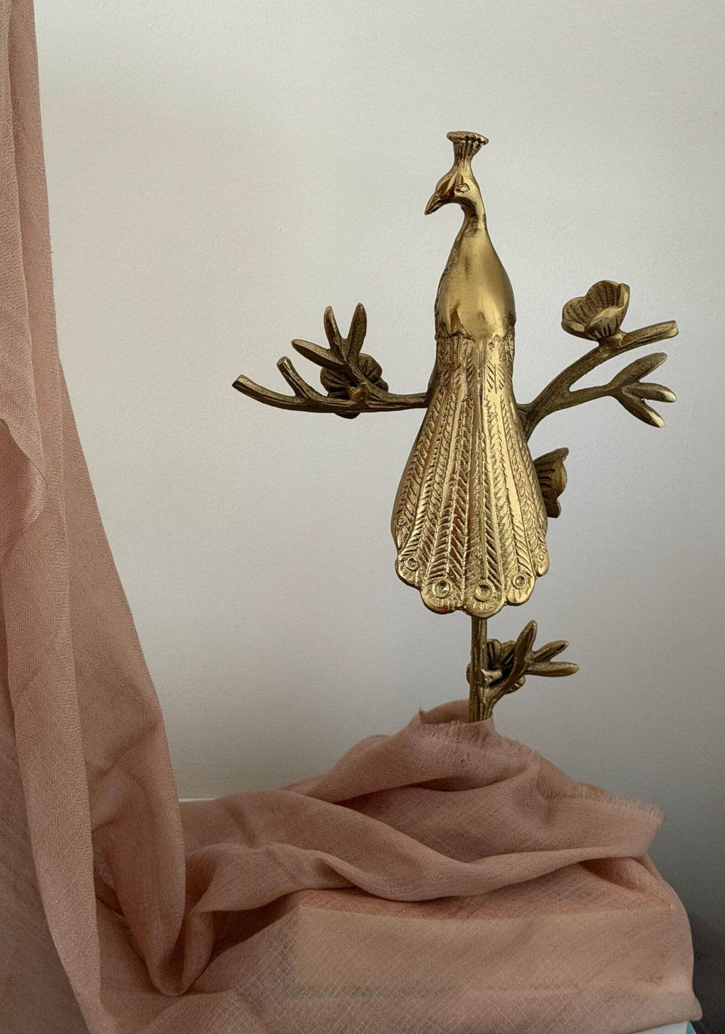 Gold peacock decorative item on a soft pink fabric background