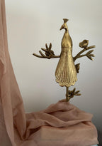 Gold peacock decorative item on a soft pink fabric background