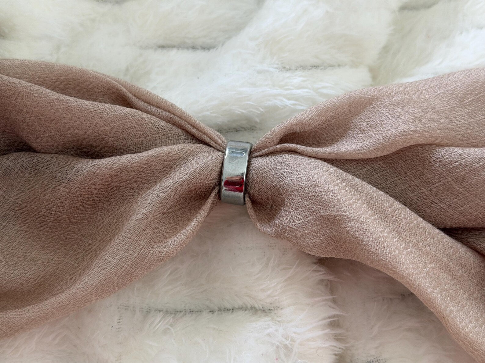 Silver ring on a knotted pink fabric with a white fur background