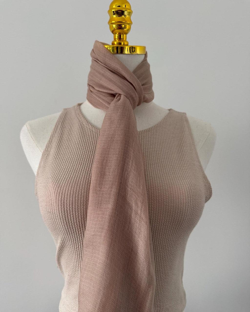 Mannequin wearing a beige ribbed sweater and pink scarf against a gray background