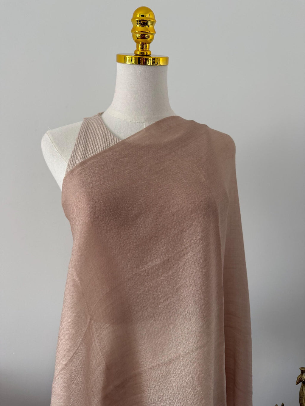 Mannequin wearing a brown draped fabric against a gray background
