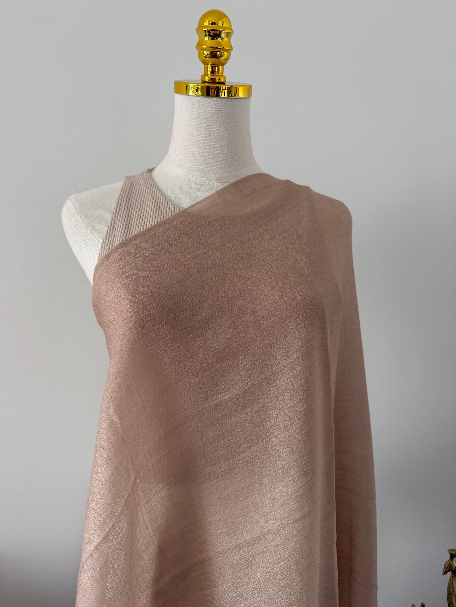 Mannequin wearing a brown draped fabric against a gray background