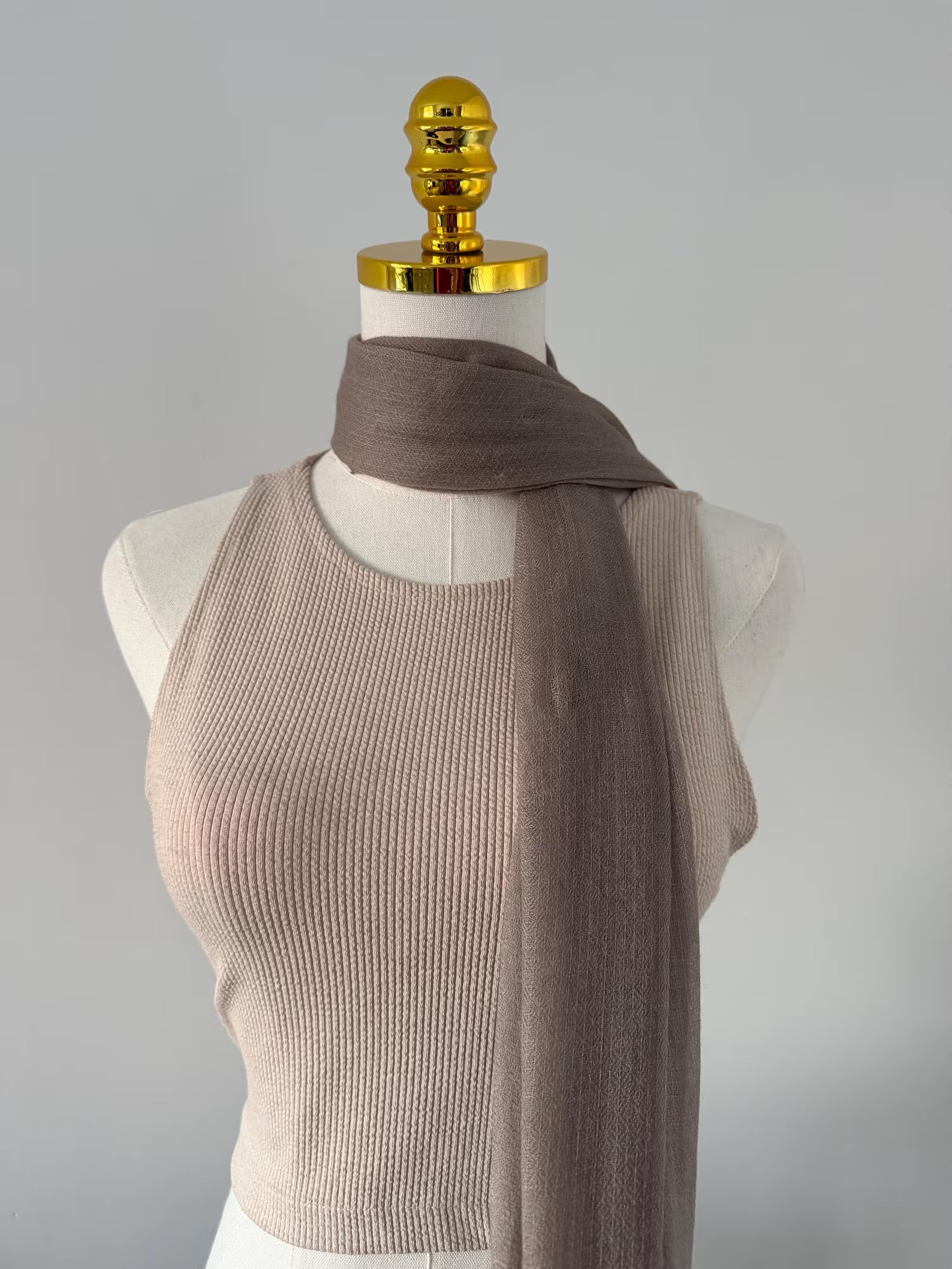 Mannequin wearing a beige ribbed top and brown scarf against a gray background