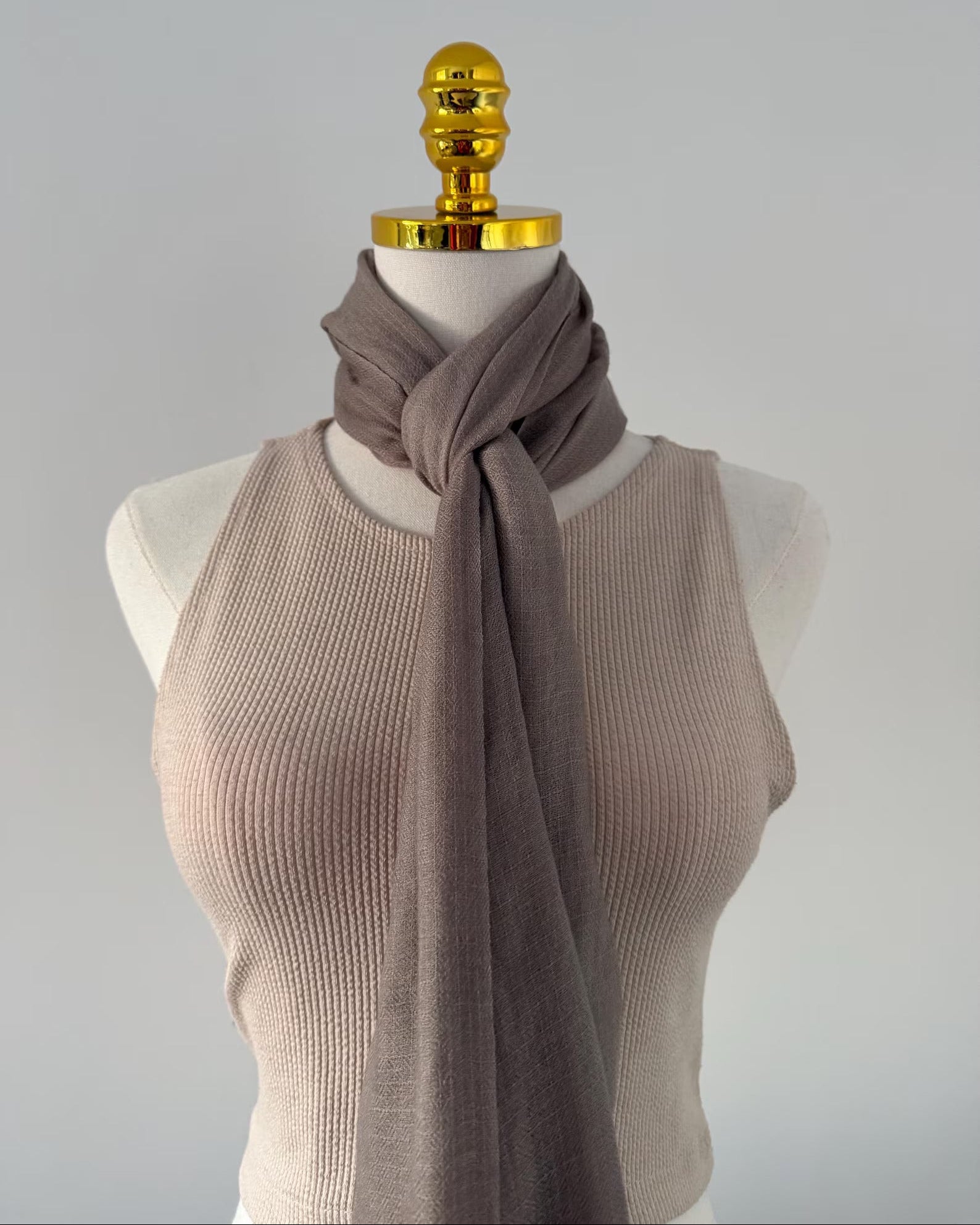 Mannequin wearing a beige ribbed sweater and brown scarf against a gray background